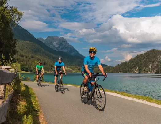 Three men on a road next to a lake riding their bicycles