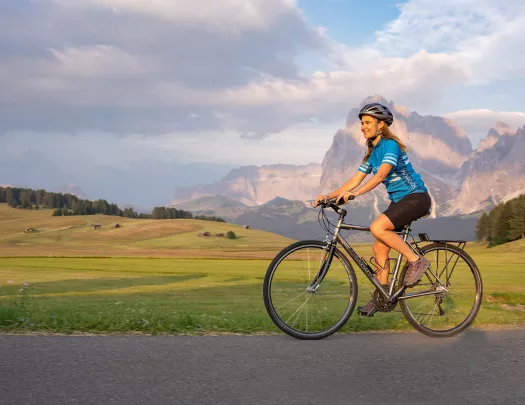 Guest cycling on road, meadow and large mountain in background.