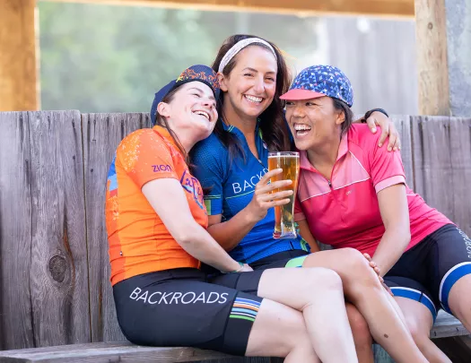 Three women smiling and hugging while holding up a glass of beer