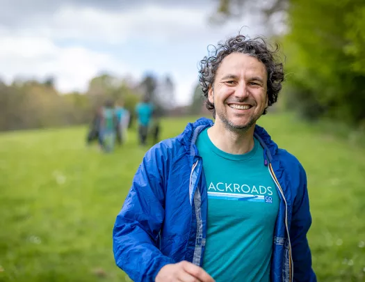 Man wearing a Backroads branded shirt, smiling with a blurry grass field behind him