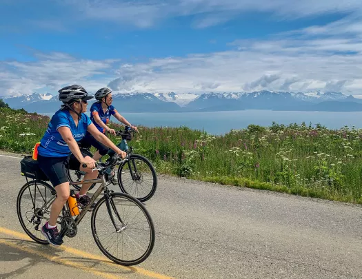 Two guests on road, cycling next to large lake. 
