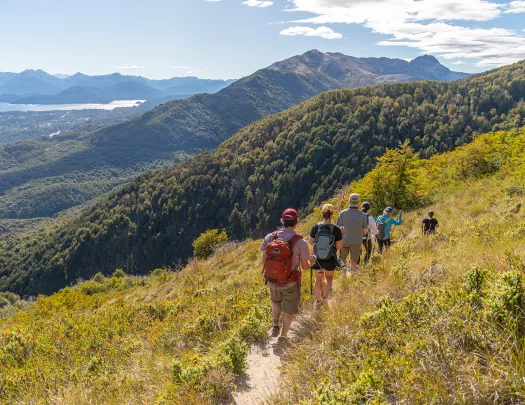 Group of guests walking down hillside, mountains, river in distance.