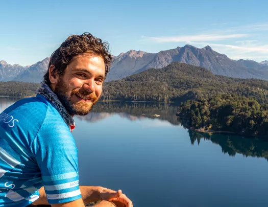 Guest posing next to still lake, forest, mountain behind them.