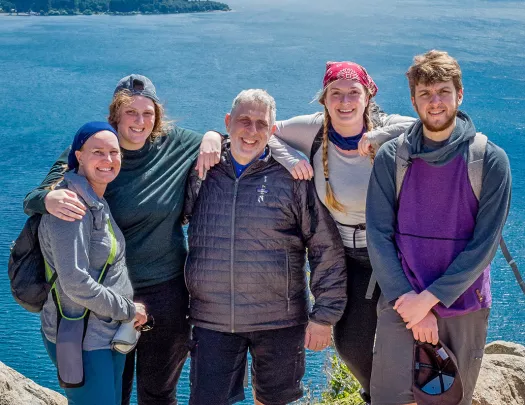 Five guests on cliffside, overlooking large lake, mountains.