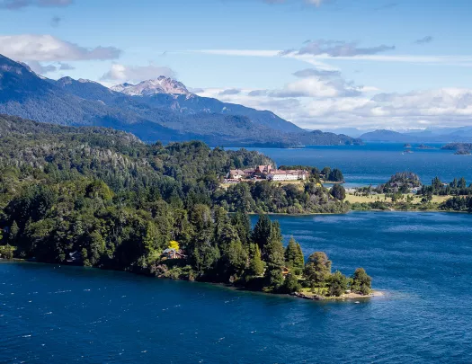 Wide shot of inlet, white building, snowy peak, larger lake in distance.