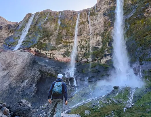Hiker looking up at a tall cliff with multiple, active waterfalls