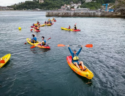 Group of guests in kayaks, one raising paddle over head, coast behind them.