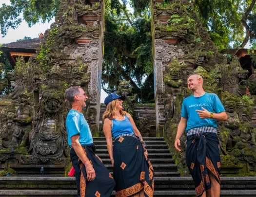 Two men and one women wearing traditional gowns in front of temple ruins