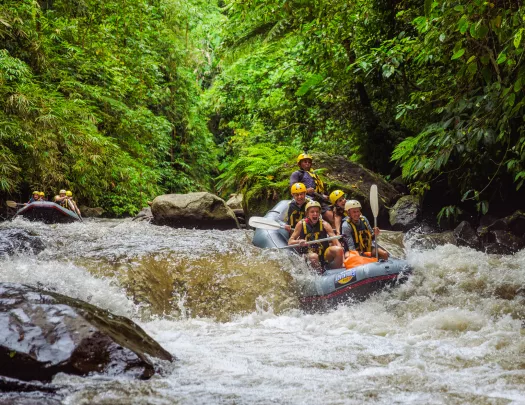 Group of people smiling while paddling on a raft through a river