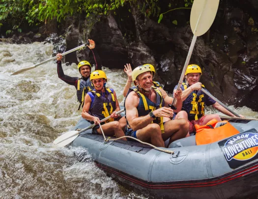 Group of people smiling and paddling in a raft in a river
