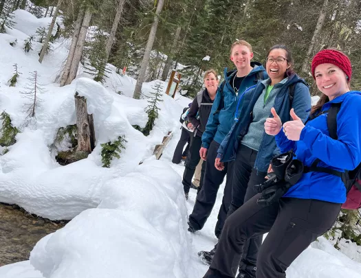 Group of people smiling with two thumbs up, in the middle of a snow patch