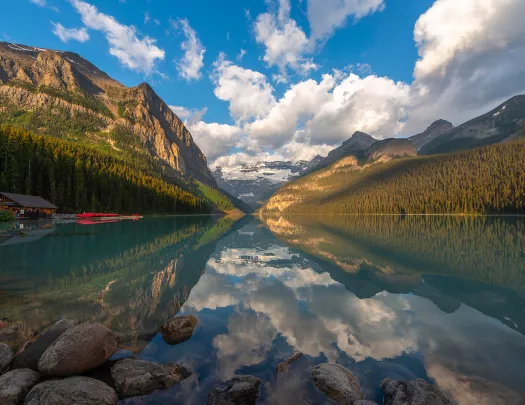 Wide shot of lake, wooden shack, mountain range, valley.