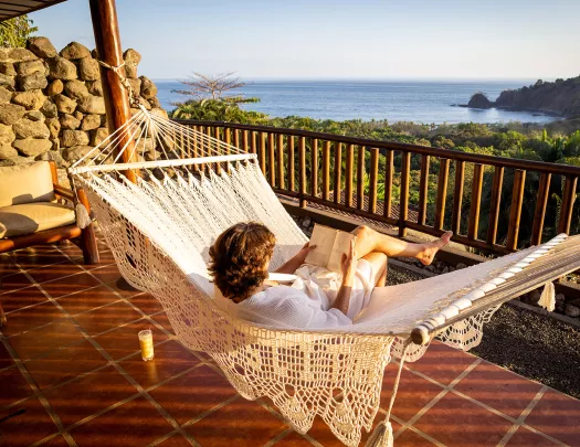 Guest on hotel balcony, hammock, overlooking forest, ocean.