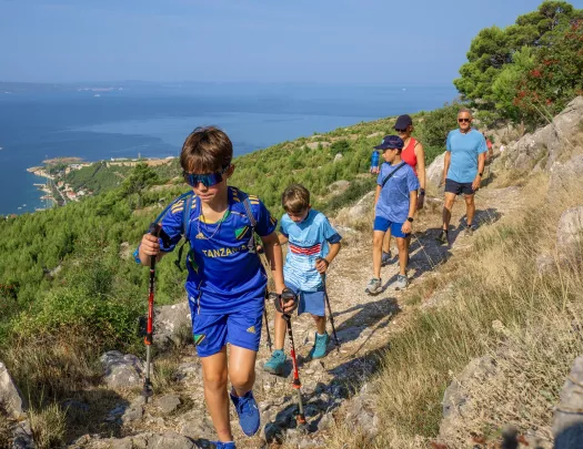 Group of kids with their parents hiking on a dirt and rock trail, with the ocean in the distance