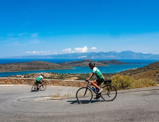 Two people riding bikes down a road, with a large lake in the distance