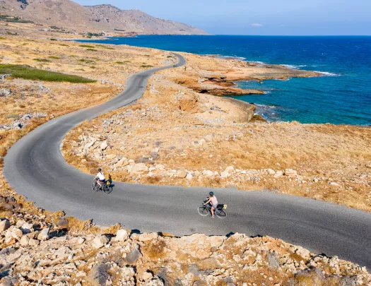 Two guests cycling along golden coastline, ocean to their right.