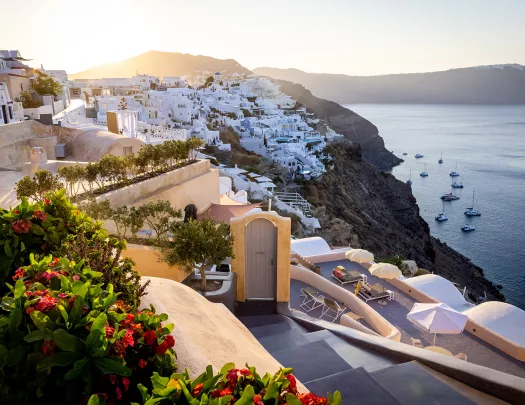 Wide shot of Santorini cliffside, white houses, ocean, sunset.