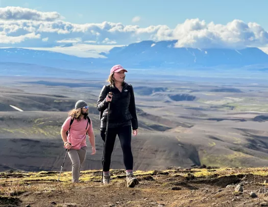 Man and woman ascending a dirt trail with large hills in the background