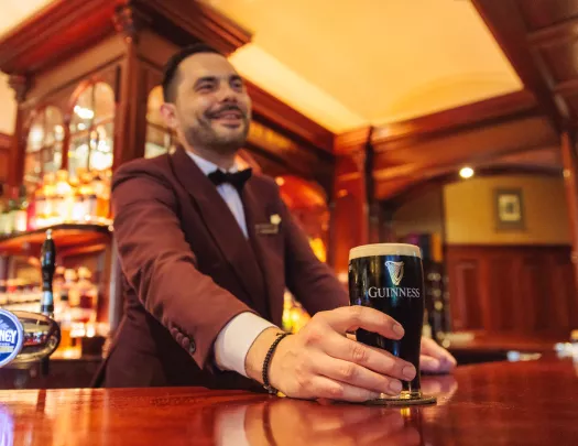 Man with a suit at a bar serving a glass of dark beer