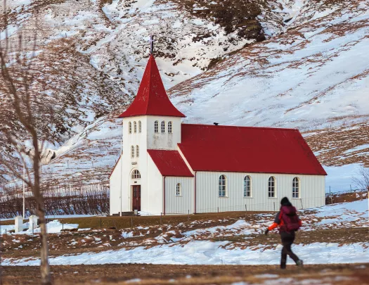 Person walking on a dirt path with a red and white church in the background