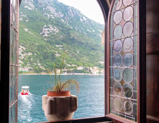 Shot from inside building, looking out window, ocean, boat, hill in background.