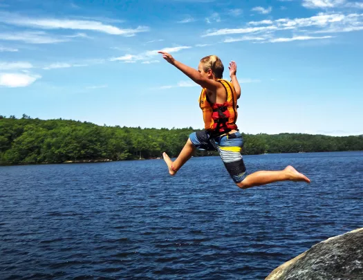 Young guest jumping from rock into lake.