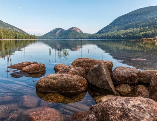 Wide shot of reflective lake, rounded mountains.