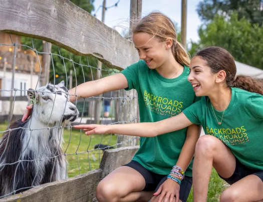 Two girls smiling while petting a goat through a fence