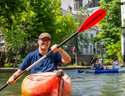 Man smiling while paddling in a red kayak on a river