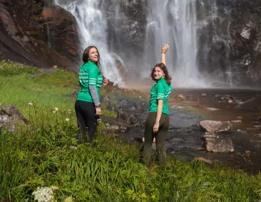 Two guests in bike jerseys pose with a waterfall