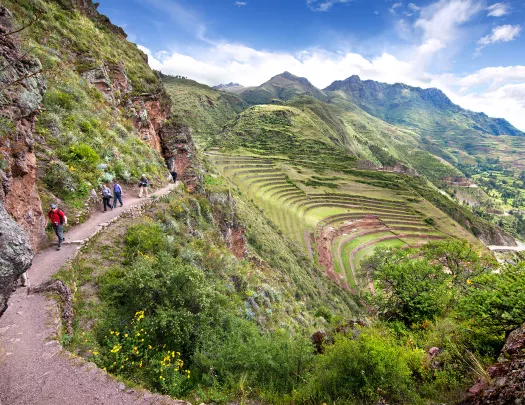 Guests hiking along cliffside trail, large sloping hillside vista next to them.