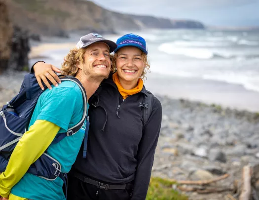 Man and woman smiling and hugging in front of a beach