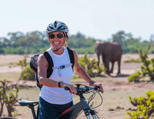 A person with a bike poses in front of an elephant