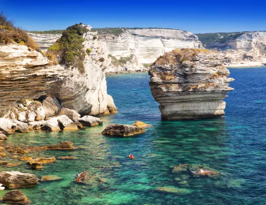 Jagged cliffs on the edge of an ocean, with a red kayak floating