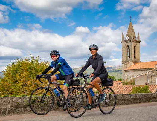 Man and woman biking on an asphalt road with a rustic clocktower in the background