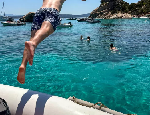 Man jumping out of a boat into a lake, with other people swimming in the ocean
