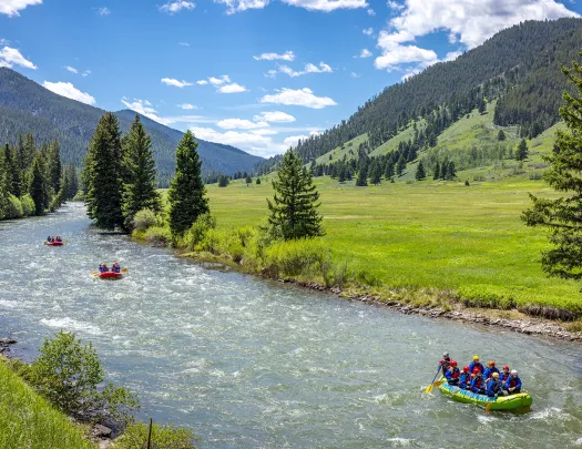 River in between two grassy valleys, with three rafts full of people