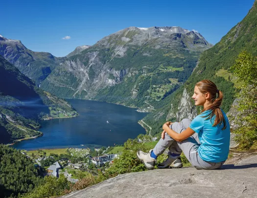 Woman sitting on a boulder, looking out to large mountains and a lake