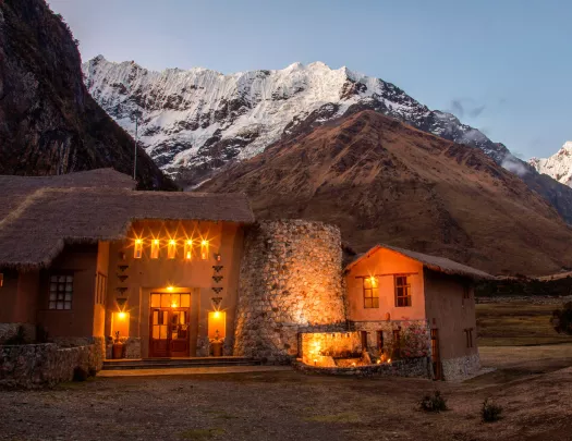 Stone building with straw roofing, with illuminated orange lights and snow-capped mountains in the backgroun