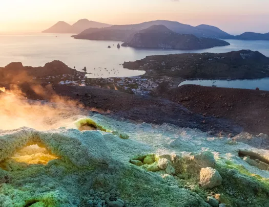 Wide shot of rocky seaside, sand deposits, water, rocky hills.