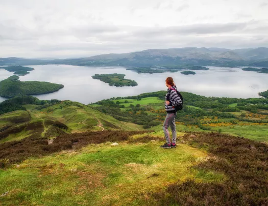 Woman standing on top of a grassy hill, looking out to smaller hills