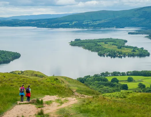 Two people descending a grassy hill towards a large lake