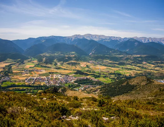 Bird's eye shot of mountainous valley, town, golden fields below.