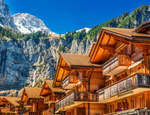 Row of wooden cabin buildings, with large mountains in the background