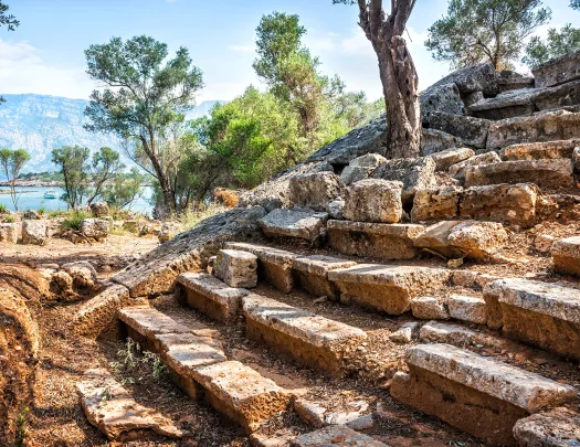 Shot of stone theater seats, trees, river, mountains behind.