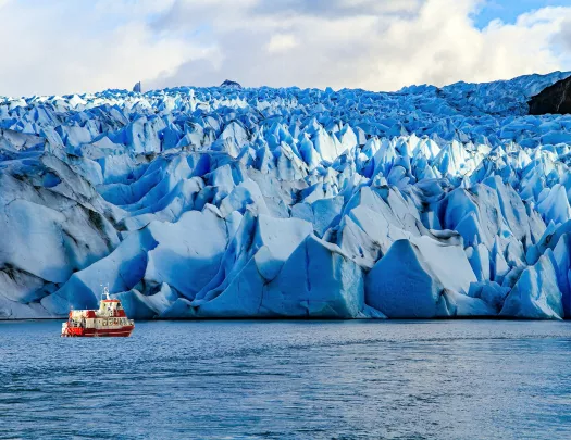 Jagged snow caps with a red and white boat traveling in front