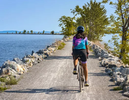 Woman riding a bike on a gravel road, surrounded by a large lake