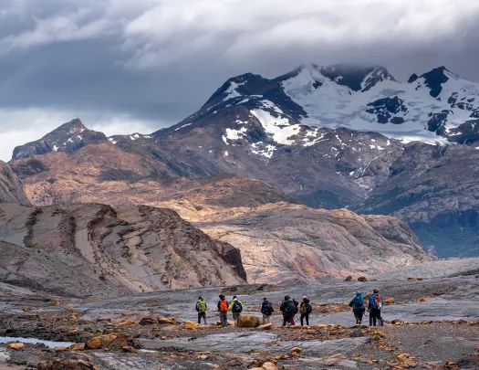 Group of guests walking among arid mountain range, snowy peaks in distance.