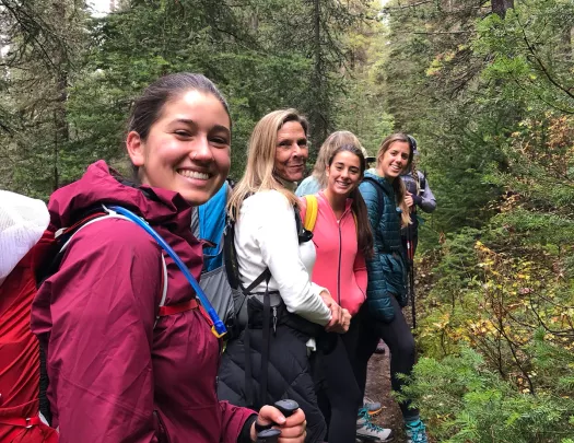 Four guests walking forest trail, all smiling at camera.