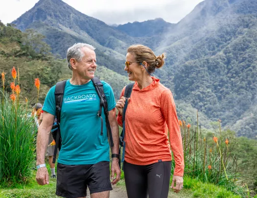 Man and woman walking on a dirt trail, with hills in the background